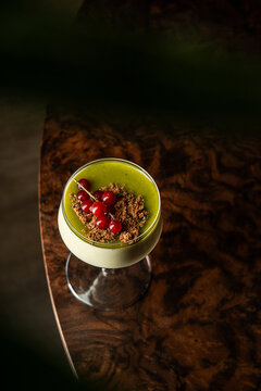 Gourmet matcha panna cotta dessert topped with cookie crumble and fresh red currants served in a cocktail glass.