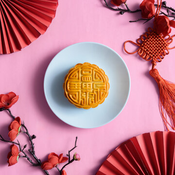 Chinese mooncake on blue plate with festive red fans and knot decor on pink background