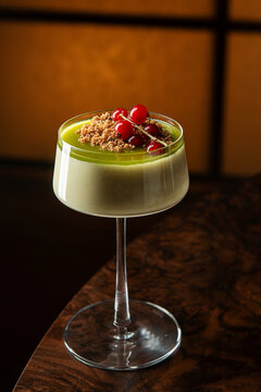 Gourmet matcha panna cotta dessert topped with cookie crumble and fresh red currants served in a cocktail glass.