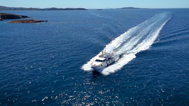 Aerial view of an modern luxury yacht cruising over the sparkling ocean leaving a trail of white surf and waves