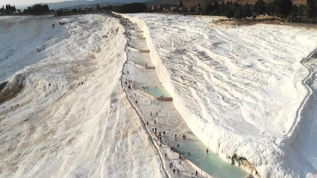 Aerial drone view of Pamukkale travertines in Turkey with tourists, white terraces, and pools.