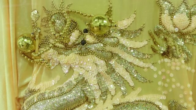 An elaborate gold and white sequin and bead embroidered dragon motif on a light-colored fabric. Shot in motion
