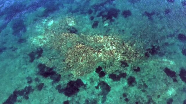 Aerial drone overhead of submerged rock and seamount in Chile with shallow turquoise water.