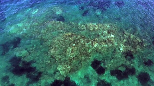 Aerial drone overhead of submerged rock and seamount in Chile with shallow turquoise water.