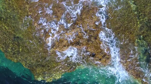 Aerial drone overhead of submerged rock and seamount in Chile with shallow turquoise water.
