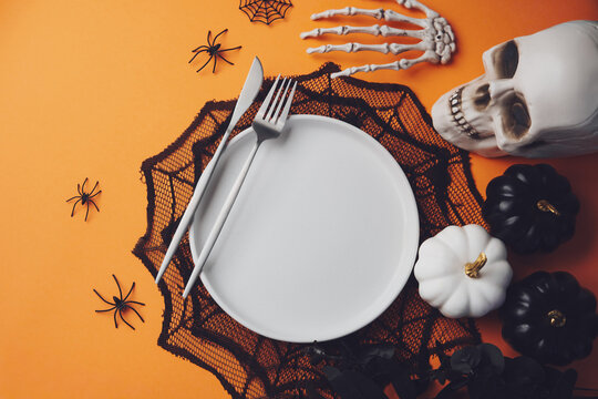 Halloween table setting with skull spiders and pumpkins on orange background