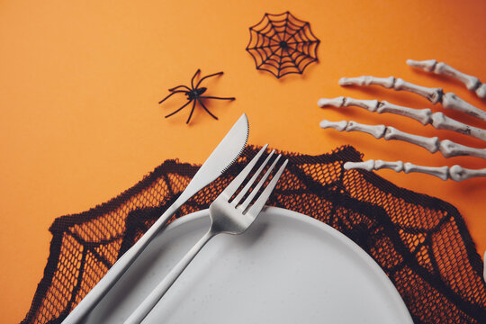 Halloween table setting with cutlery and spider decorations on orange background