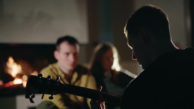 Silhouetted Guitarist Playing by a Fireplace