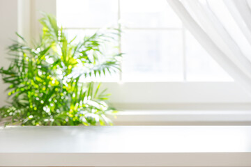 Fototapeta premium White table top with blurred green plant near a sunny window background