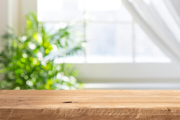 Naklejka premium Wooden table top with blurred green plant and window background