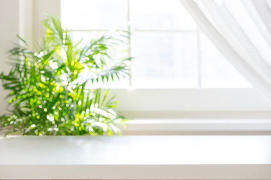 White table top with blurred green plant near a sunny window background