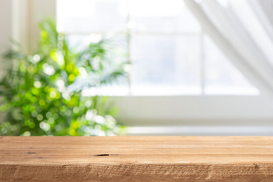Wooden table top with blurred green plant and window background