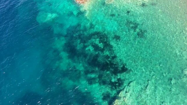 Aerial drone view of layered coastal rock and fault like strata beside clear ocean water.