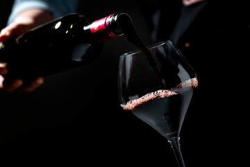 Obraz premium Authentic Malbec red wine splashing in glass — gourmet lifestyle concept. Restaurant sommelier with dark bottle pouring alcoholic beverage. Hospitality industry, fine dining celebration.
