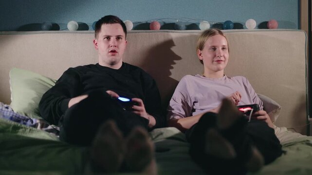Two Young Adults Playing Video Games on a Bed
