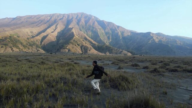 4K video of a man running across savannah grassland with majestic mountain background in Indonesia.