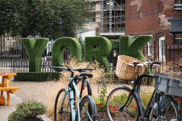 Fototapeta premium York letters crafted from lush green topiary standing prominently in a public park, with bicycles parked nearby suggesting urban exploration and sustainable travel