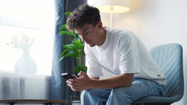 Young smiling man texting on a smartphone at home
