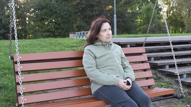 Pensive Woman Swinging on Swing in City Park.

