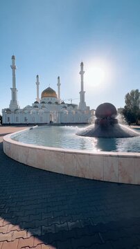 Abu Nasr Al-Farabi Mosque behind fountain basin in Astana, with golden dome, slender minarets, reflective water and spacious plaza, shot handheld, vertical video, 4k footage