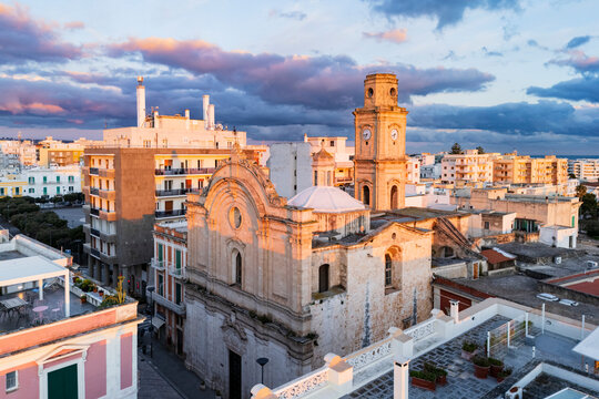 Church clock tower over rooftops at sunrise in monopoli, Italy