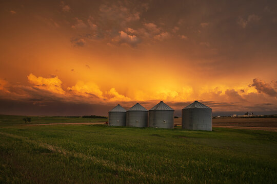 Sunset over grain silos in south dakota farm field with storm clouds