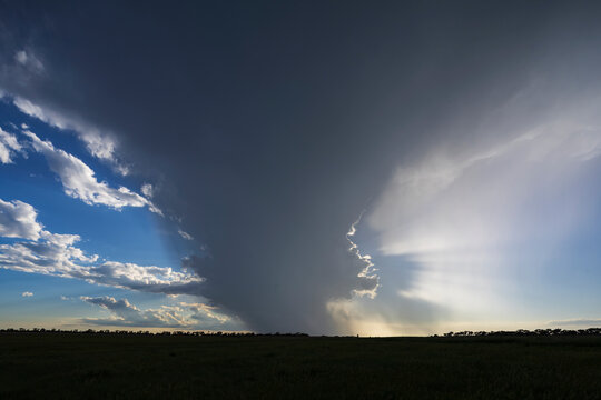 Storm with dark clouds and sunlight over flat field