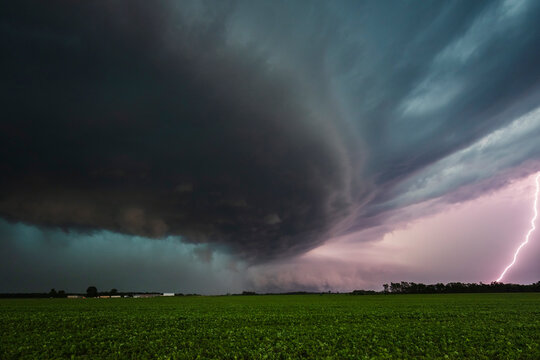 Supercell storm with lightning striking over a green field
