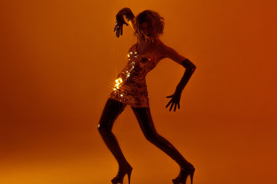 Dancing woman in gold sequin dress, expressive pose in amber light, dark fashion silhouette