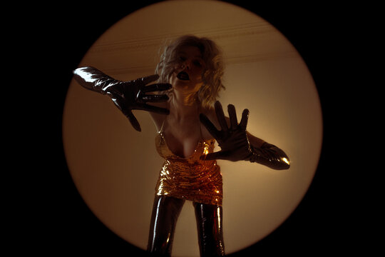 Surreal round frame, woman in gold sequins reaching gloved hands toward camera, dark vignette