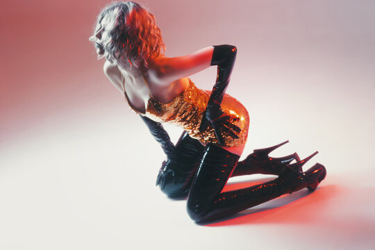 Pop style fashion, kneeling woman in gold sequins on pink to white gradient, high key light