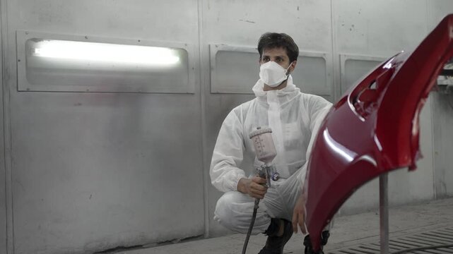 Latin Mechanic Spray Painting Red Car Part In Auto Body Repair Shop
