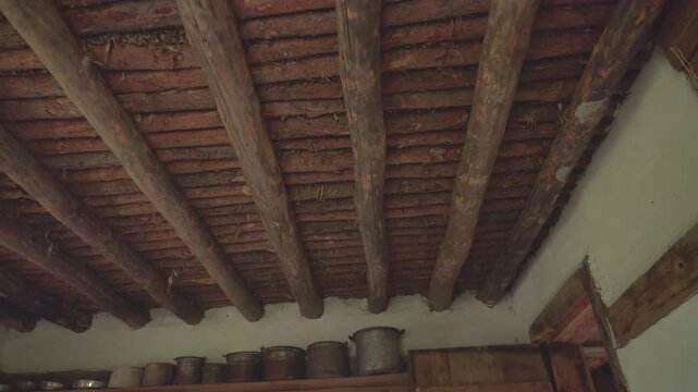 Old wooden ceiling made from tree logs covers a poor historic rural house interior.