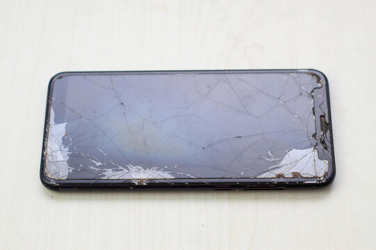 smartphone with badly broken and cracked glass screen on white table