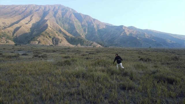 4K video of a man running across savannah grassland with majestic mountain background in Indonesia.