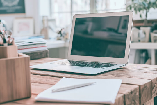 Laptop computer open on wooden desk at low diagonal angle with notebook and pen