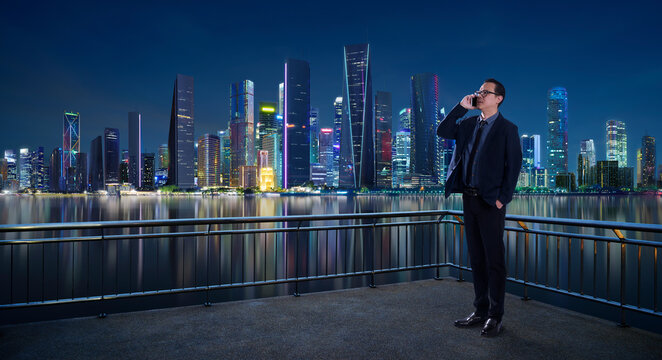 Businessman talking on smartphone with city skyline at night