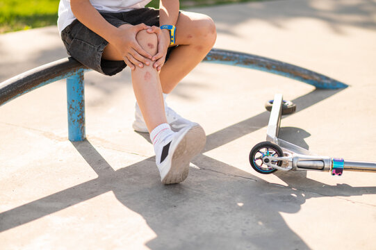 Boy in a hat sitting on the ground near the scooter after a fall down