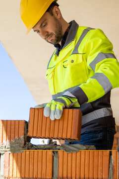 Professional mason wearing safety gloves placing orange ceramic block