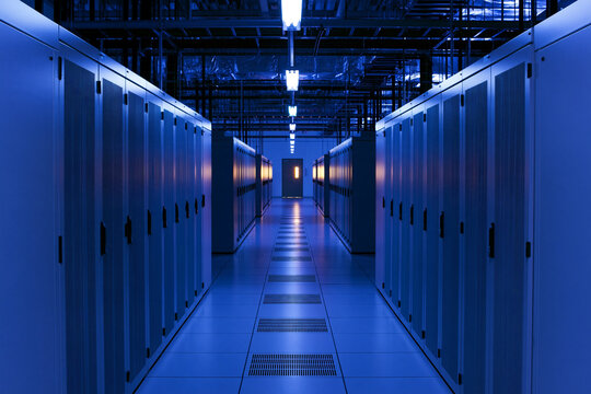 Data center aisle lined with cabinets under cool blue lighting, cloud hosting concept