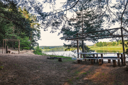 Scenic campsite with wooden pergola and table overlooking river Neman. Natural shelter for picnics and gathering near water. Outdoor activities, camping, weekend, rural tourism.