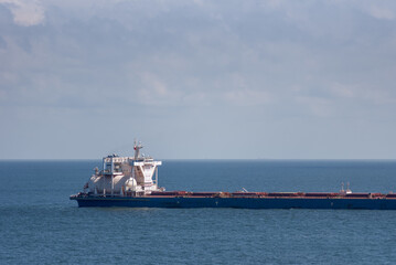 Fototapeta premium Large LNG-powered bulk carrier sailing slowly across calm blue waters, with the distinctive LNG fuel tank visible near the superstructure.