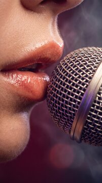 Extreme close-up of lips at a microphone grid with dark, colorful bokeh