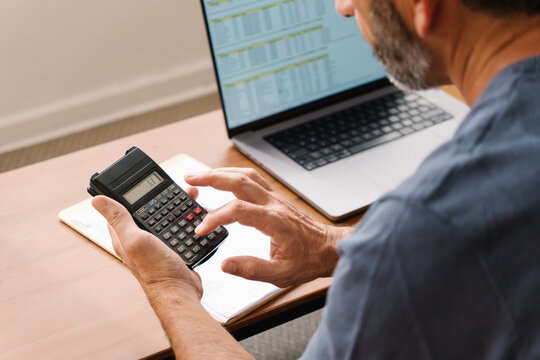Man using handheld calculator and laptop during calculation task in busy office desk