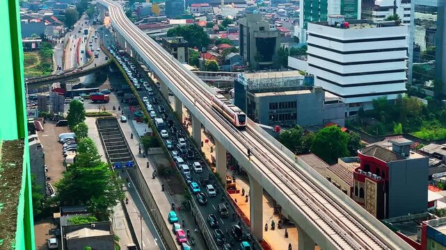 LRT train moves overhead, cutting through urban grid. Cars flow below, a constant hum of daily life. Aerial view captures city's rhythm, blending transit and traffic.
