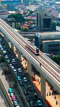 LRT train moves overhead, cutting through urban grid. Cars flow below, a constant hum of daily life. Aerial view captures city's rhythm, blending transit and traffic.