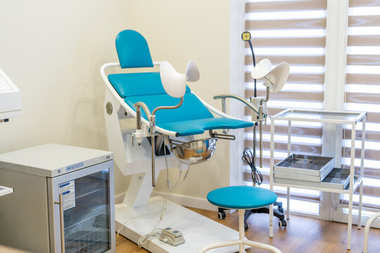 Interior of a modern, bright, and clean gynecological office featuring a teal examination chair equipped with stirrups.