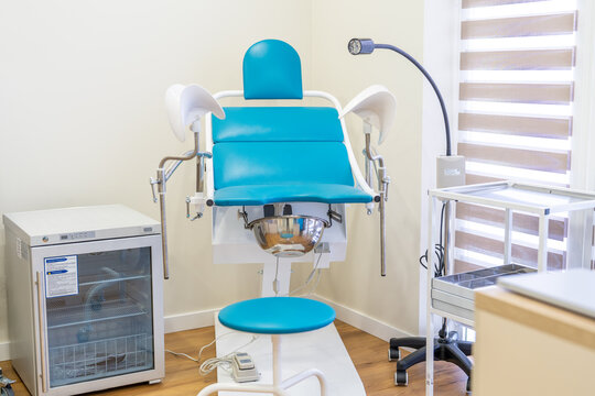 Interior of a modern, bright, and clean gynecological office featuring a teal examination chair equipped with stirrups.