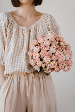 Elegant model wearing beige linen outfit holding beautiful pink flower arrangement carefully