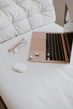 Elegant workspace with laptop, glasses, and earbuds on a white bed